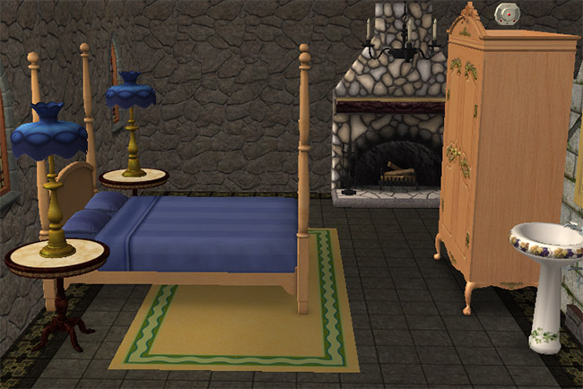 A stone bedroom with a blue bed, fireplace, tall candle stands, a green rug, and a light wood wardrobe.
