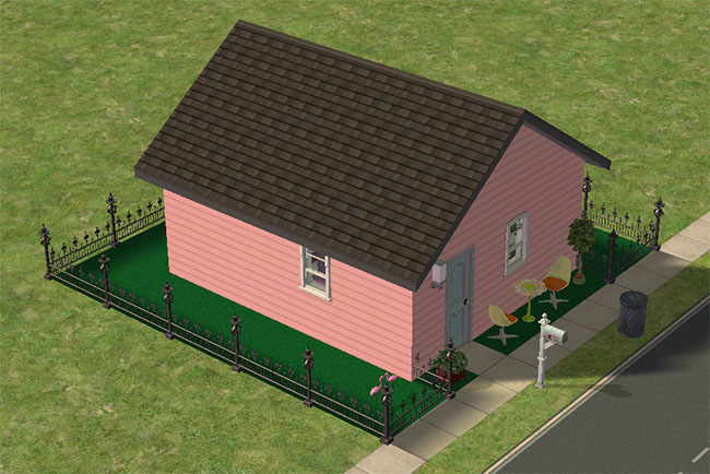An angled front view shows the pink one-room house on a fenced astroturf lot with patio seating, potted plants, a mailbox, sidewalk access, and a dark sloped roof.